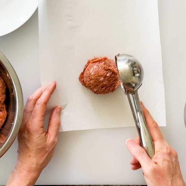 Scooping a ball of ground turkey a sheet of parchment paper.