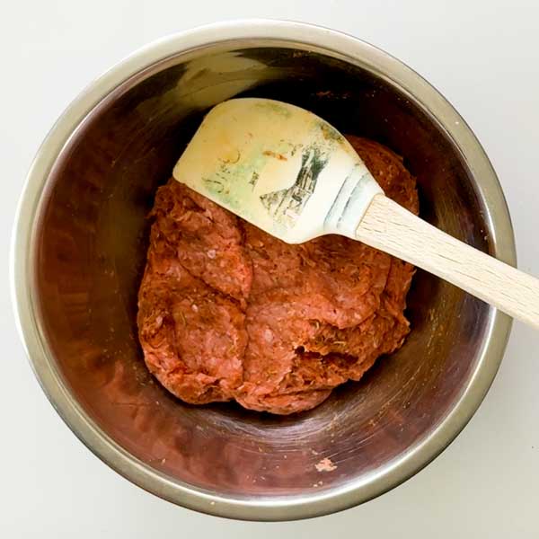 Stirring the ground turkey into the seasonings in a mixing bowl with a spatula.