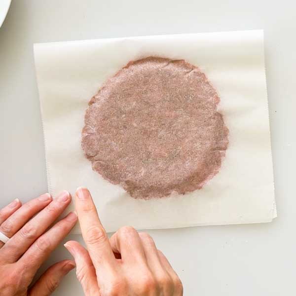 Pressing the ground turkey ball between two pieces of parchment paper with a flat dish.