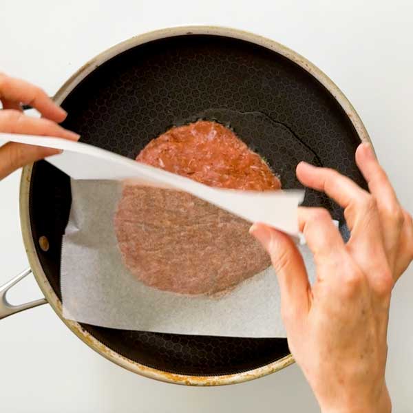 Laying the ground turkey patty into the skillet using parchment paper.
