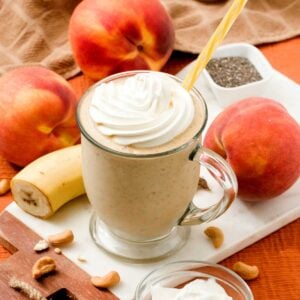 A high protein peaches and cream protein smoothie in a glass with a straw.
