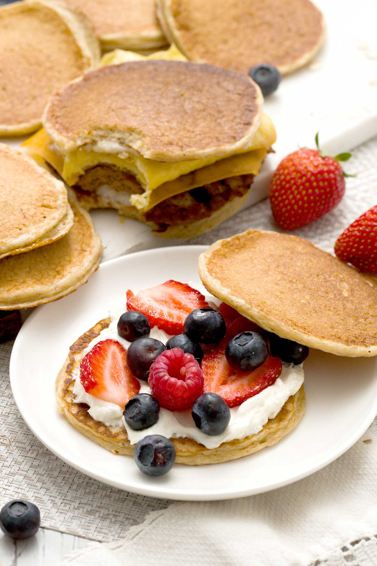 An open-face, gluten-free protein pancake sandwich with oat flour and filled with cream cheese and berries, and sausage, eggs, and cheese.