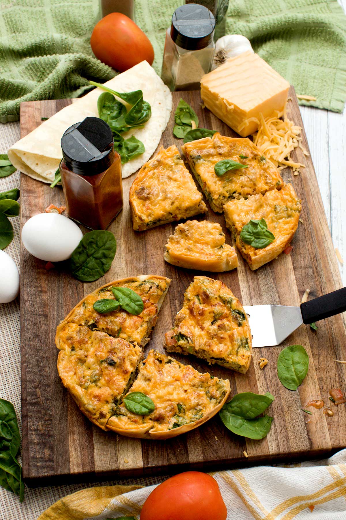 Two high-protein tortilla quiches with spinach, tomatoes, cheese on a cutting board.