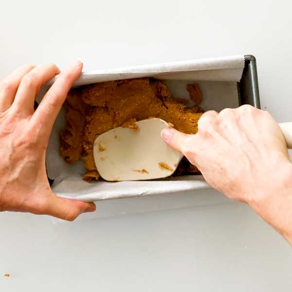 Pressing the protein bar dough into a parchment paper lined bread pan.