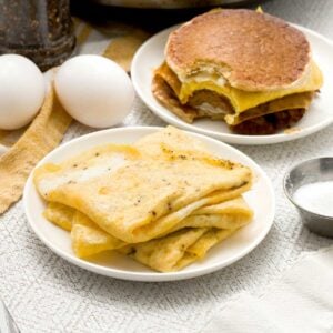 Three folded egg omelets on a plate next to a breakfast sandwich.