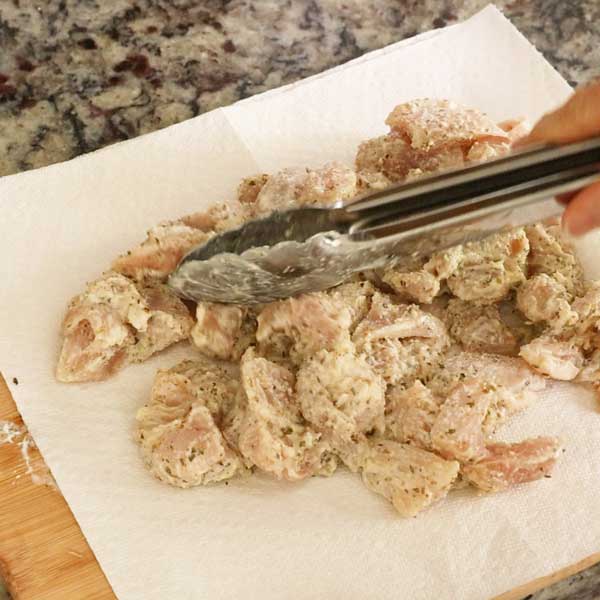 Dabbing off the excess moisture from the marinated chicken pieces with a paper towel.