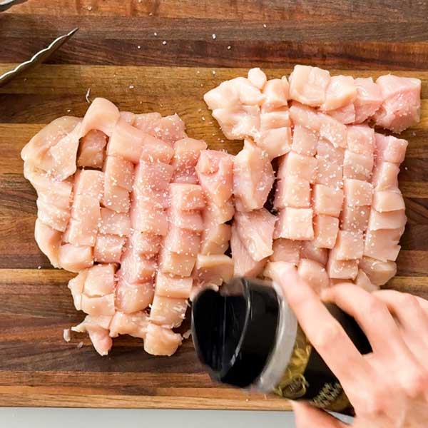 Seasoning the chopped chicken breasts with salt.