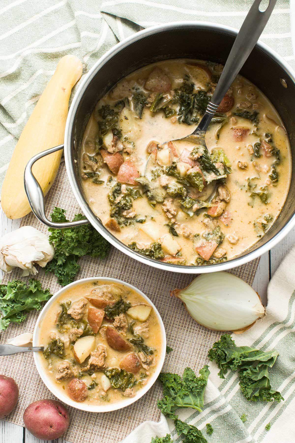 A bowl of healthy Zuppa Tuscana soup with ground turkey and greek yogurt with red potatoes next to a Hexclad pot.