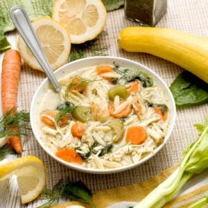 A bowl of seared lemon chicken orzo soup with yellow squash and spinach.