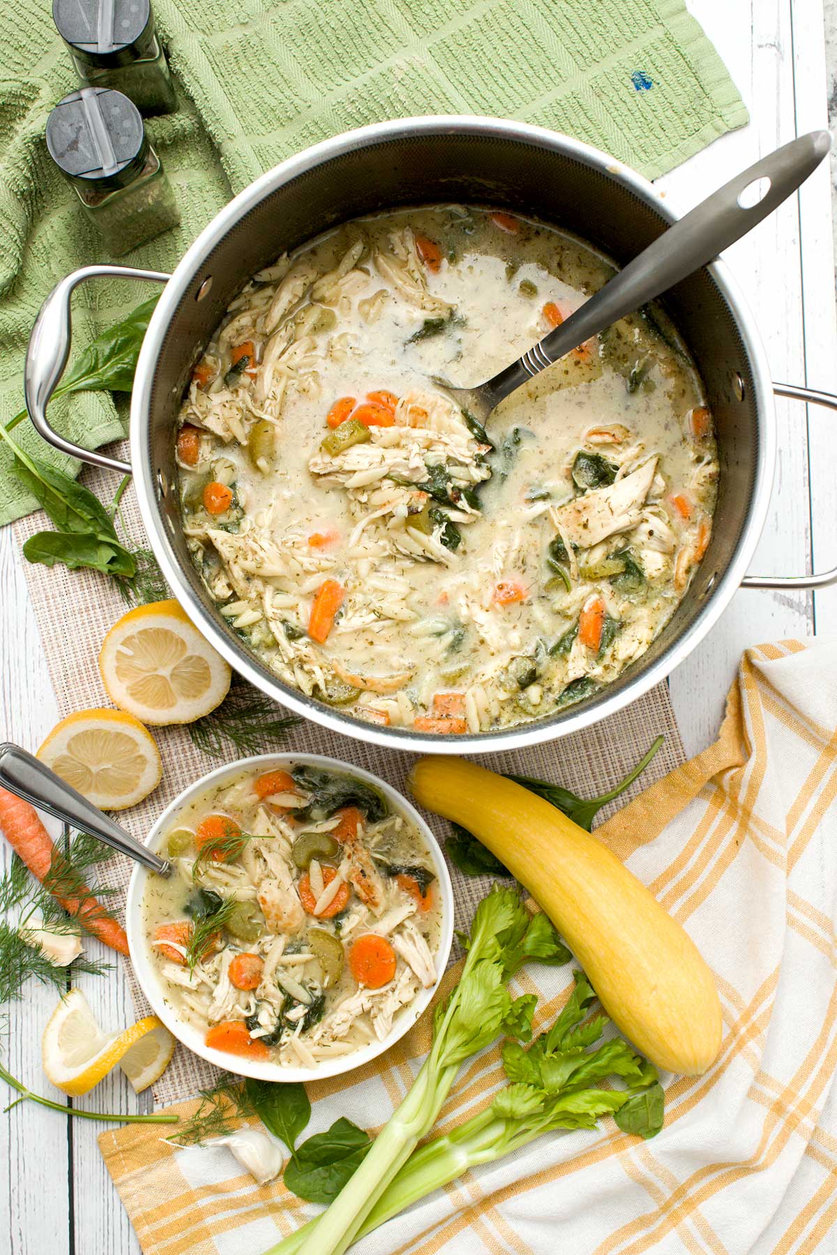 A pot and bowl of seared lemon chicken orzo soup with yellow squash and spinach.