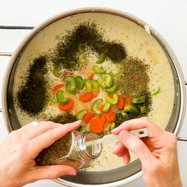 Adding the carrots, celery, and seasonings to the soup.