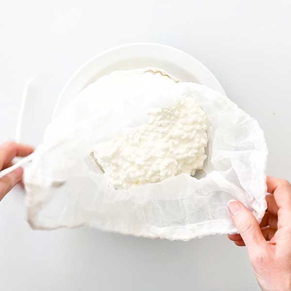Adding the cottage cheese to a strainer bag.