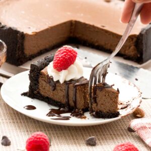 A slice of gluten-free chocolate cheesecake with cottage cheese and protein powder with whipped cream and a raspberry on top.