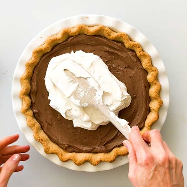 Spreading whipped topping on top of the pie.