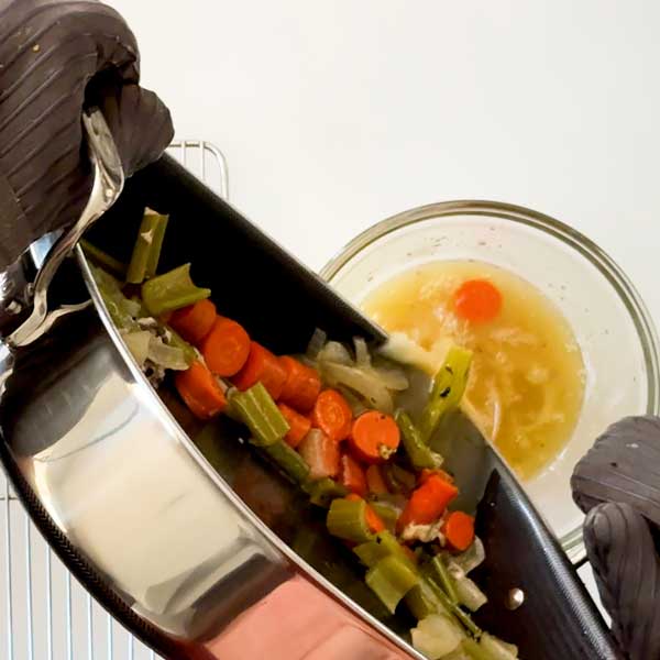 Pouring the vegetables and drippings from the roasting pan into a mixing bowl.