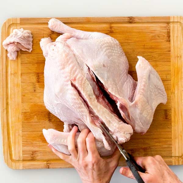 Cutting the spine out of the turkey with strong kitchen shears.
