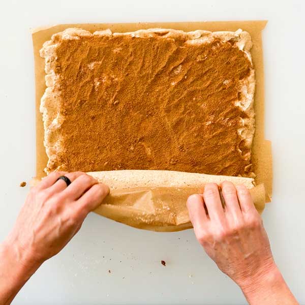 Rolling the cinnamon roll dough with the parchment paper.
