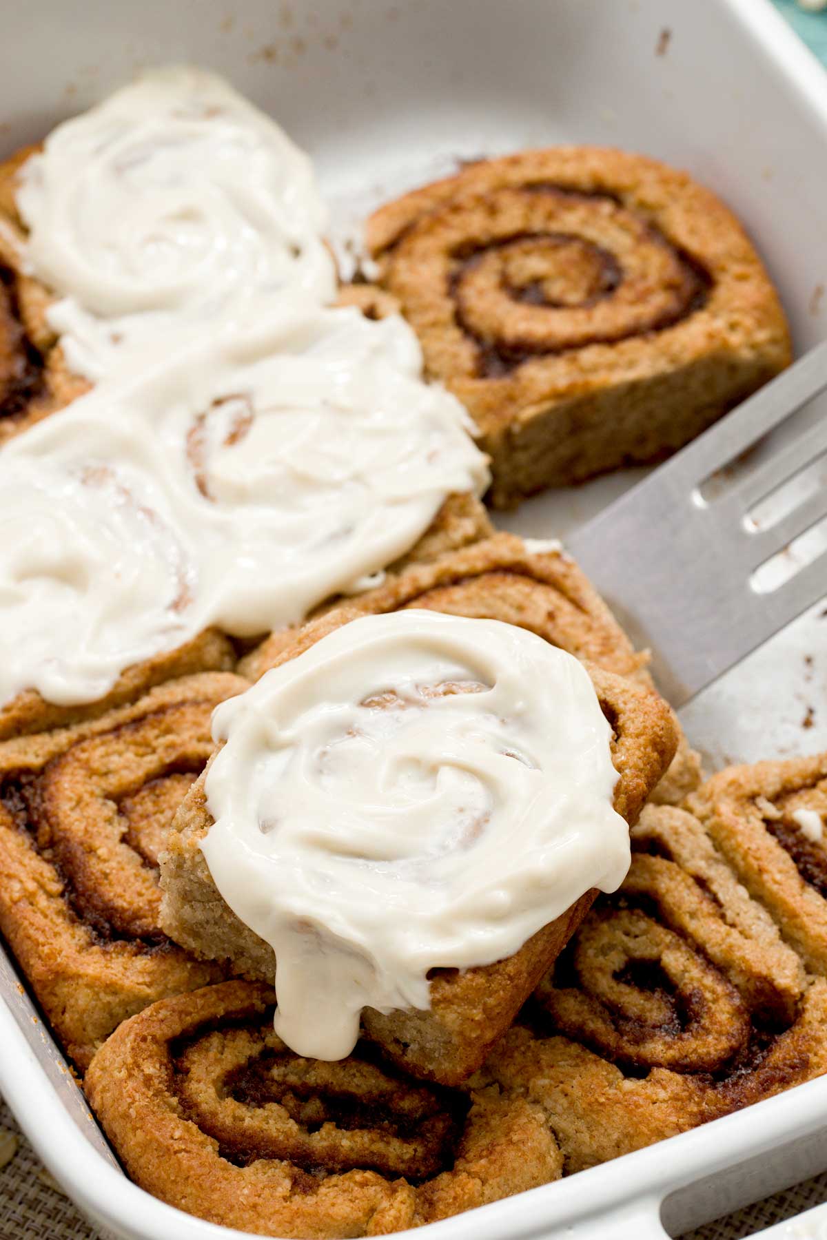 A close-up of a pan of gluten-free cottage cheese cinnamon rolls with a maple cream cheese spread on top.