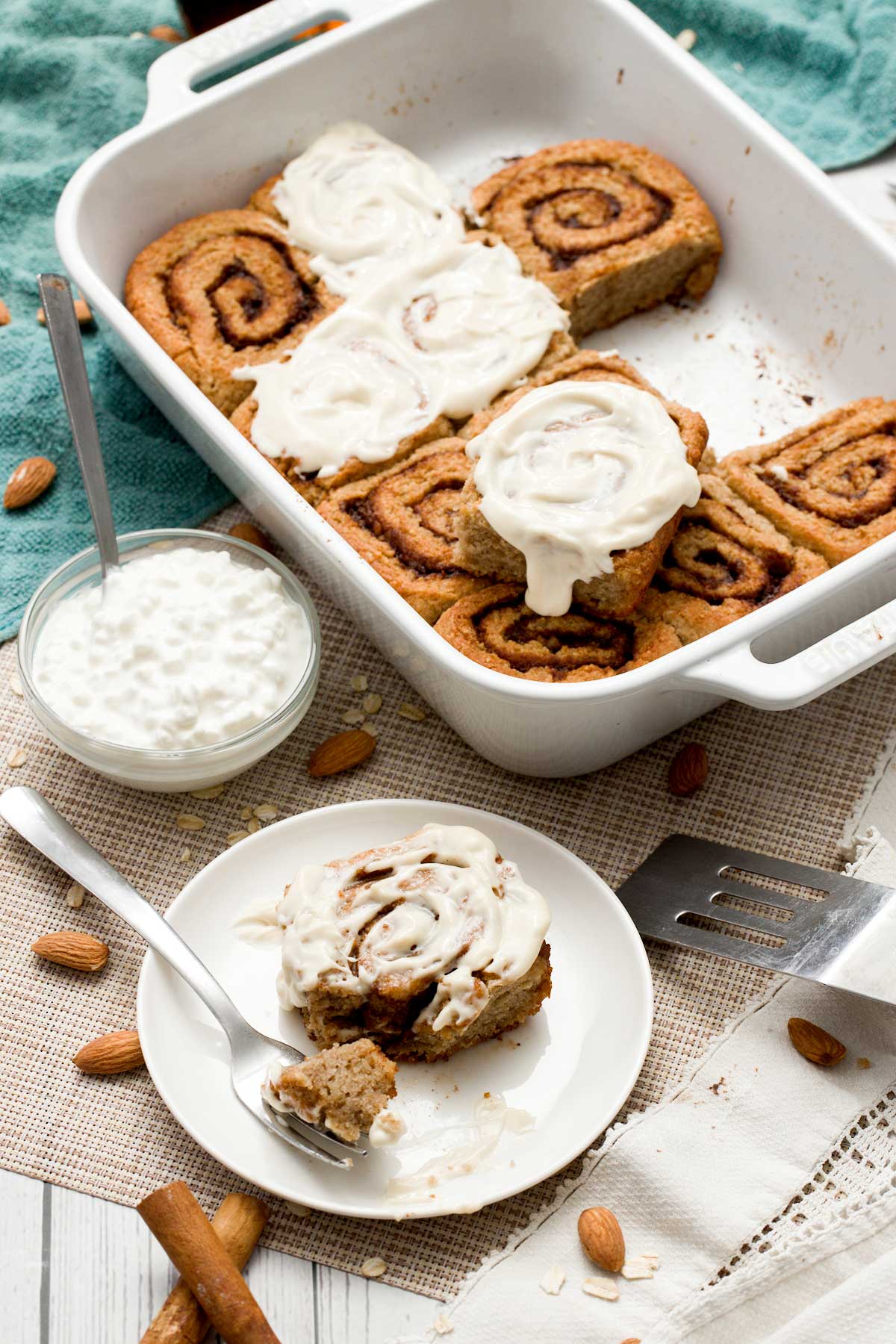 A pan and plate with gluten-free cottage cheese cinnamon rolls with a maple cream cheese spread on top.