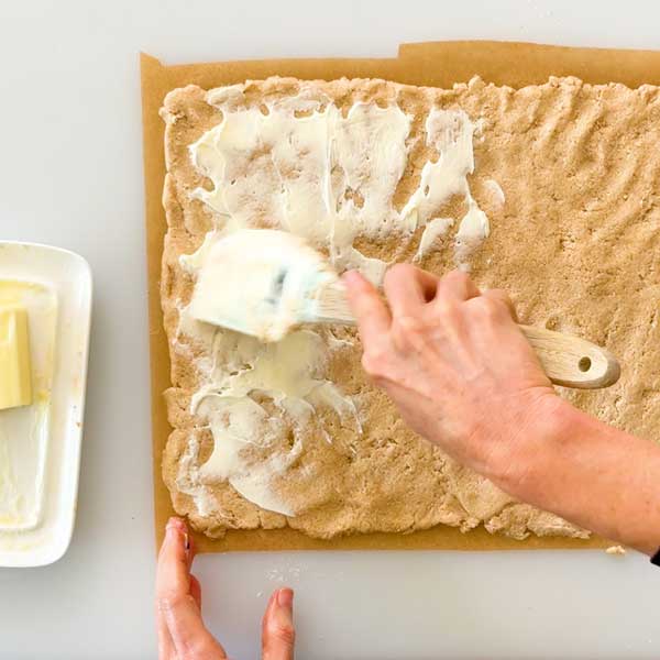 Spreading soft room temperature butter on the cinnamon roll dough.