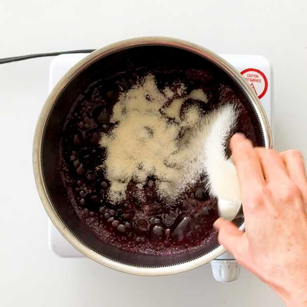 Adding the sugar to the cherries in the saucepan.