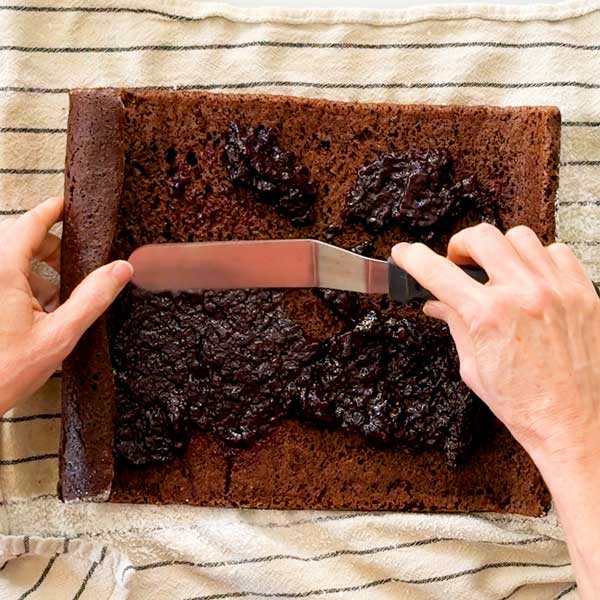 Spreading the cherry compote over the cooled and unrolled cake.