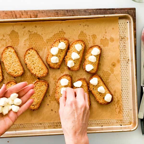 Adding mozzarella cheese to the crostinis.