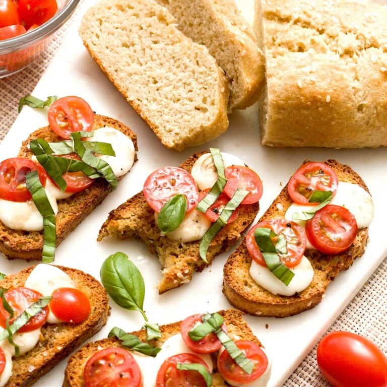 A loaf of no-yeast bread next to gluten-free crostinis with tomato, basil, and mozzarella cheese.