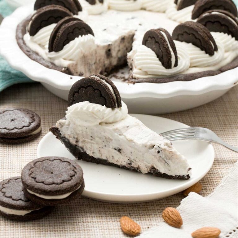 A gluten-free oreo cream pie with whipped cream on top and a slice on a plate.