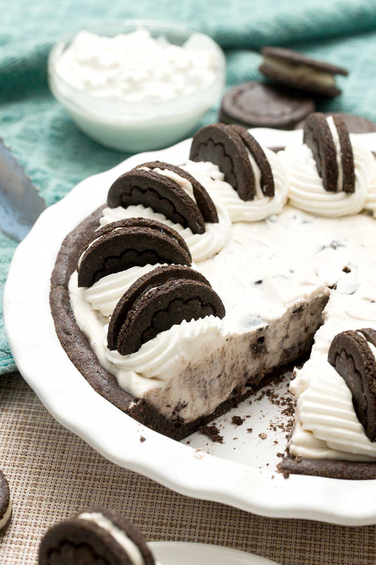 A close-up view of a gluten-free oreo cream pie with whipped cream on top missing a slice.