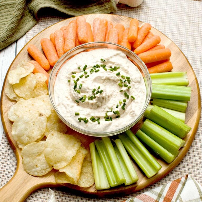 A bowl of french onion dip with greek yogurt surrounded by cut veggies and potato chips.