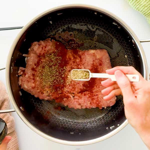 Adding the seasonings to the top of the ground chicken in the pot.