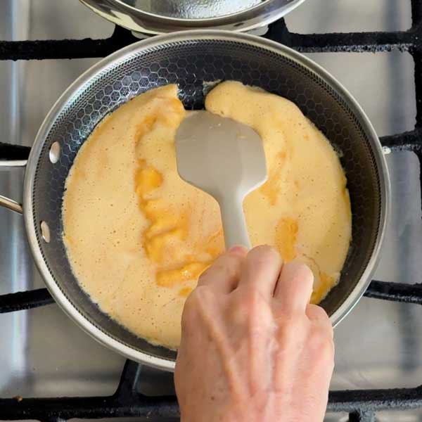 Dragging the cooked edges of the omelet to the center of the skillet.