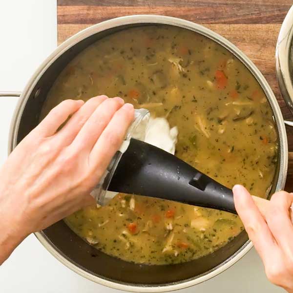 Stirring the greek yogurt into the cooked soup after it's been taken off the heat.