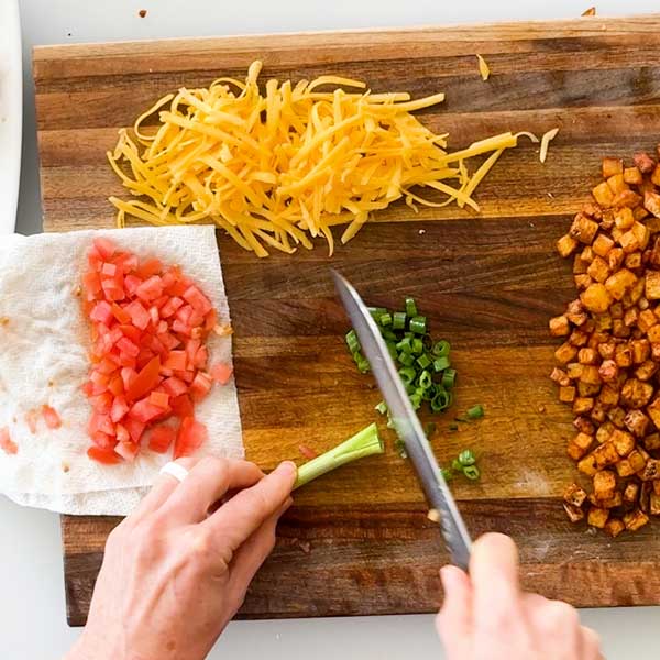 Dicing the green onion and tomatoes on a cutting board.